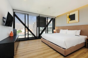 Ein modernes Hotelzimmer mit einem großen Bett, einem Fernseher, einem Schreibtisch und Blick auf die Stadt.