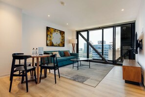 A modern living room with a sofa, coffee table, and chairs, a painting on the wall, and a large window with a city view. - w Amazing 1BR w/ AC in the Heart of Roma Sur (Mexico City)