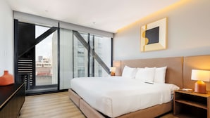 A modern hotel room with a large bed, a desk, a chair, a lamp, and a view of the city through a large window. - w Amazing 1BR w/ AC in the Heart of Roma Sur (Mexico City)
