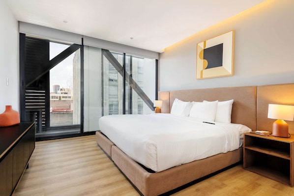 A modern hotel room with a large bed, a desk, a chair, a lamp, and a view of the city through large windows. - w Amazing 1BR w/ AC in the Heart of Roma Sur (Mexico City)
