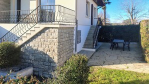 A two-story house with a stone staircase, a balcony with metal railings, and a patio area with a table and chairs. - Spacious apartment near ocean and shops (Angresse)