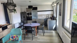 A compact kitchen with modern appliances, a dining area with a round table and chairs, and a large window providing natural light. - Spacious apartment near ocean and shops (Angresse)