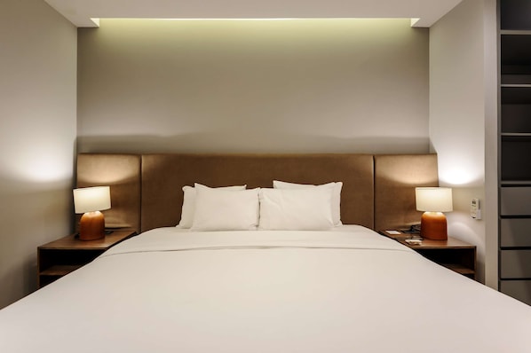 Ein Hotelzimmer mit einem großen Bett, zwei Nachttischen mit Lampen, einer Kopfteil und einem Wandregal.
