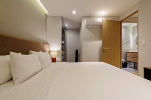 Ein Hotelzimmer mit einem großen Bett, einem Nachttisch mit Lampe, einem Kleiderschrank und einer Klimaanlage.