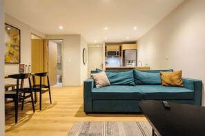 Ein Wohnzimmer mit einem türkisfarbenen Sofa, einem Couchtisch und einem Essbereich mit Stühlen.