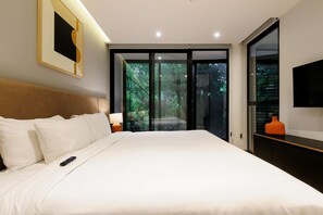 Ein Schlafzimmer mit einem Bett, einer Fernbedienung, einem Nachttisch, einer Lampe, einem Fernseher und einer Schiebetür, die zu einem Balkon mit Blick auf Bäume führt.