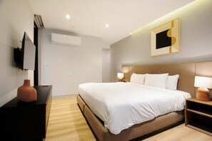 Ein modernes Hotelzimmer mit einem großen Bett, Nachttischlampen, einem Flachbildfernseher und einer Wand-Klimaanlage.