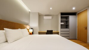 Quarto de hotel com uma cama grande, escrivaninha, cadeira, guarda-roupa e ar condicionado.