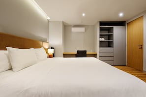 Ein Hotelzimmer mit einem großen Bett, einem Schreibtisch, einem Stuhl, einem Kleiderschrank und einer Klimaanlage.