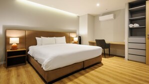 Quarto de hotel com uma cama grande, mesas de cabeceira, escrivaninha, cadeira e guarda-roupa.