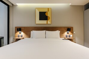 Ein Hotelzimmer mit einem großen Bett, einem Holzkopfteil, zwei Nachttischen mit Lampen, einem Wandbild und einem Fenster.