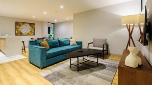 Uma sala de estar moderna com um sofá azul-turquesa, uma mesa de centro, uma mesinha de cabeceira de madeira e um abajur.