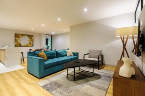 Ein modernes Wohnzimmer mit einem türkisfarbenen Sofa, einem Couchtisch, einem Holznachttisch und einer Lampe.