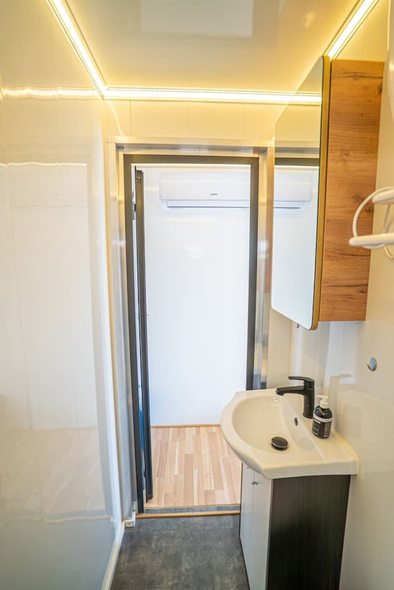 A compact bathroom with a shower, sink, and mirror.