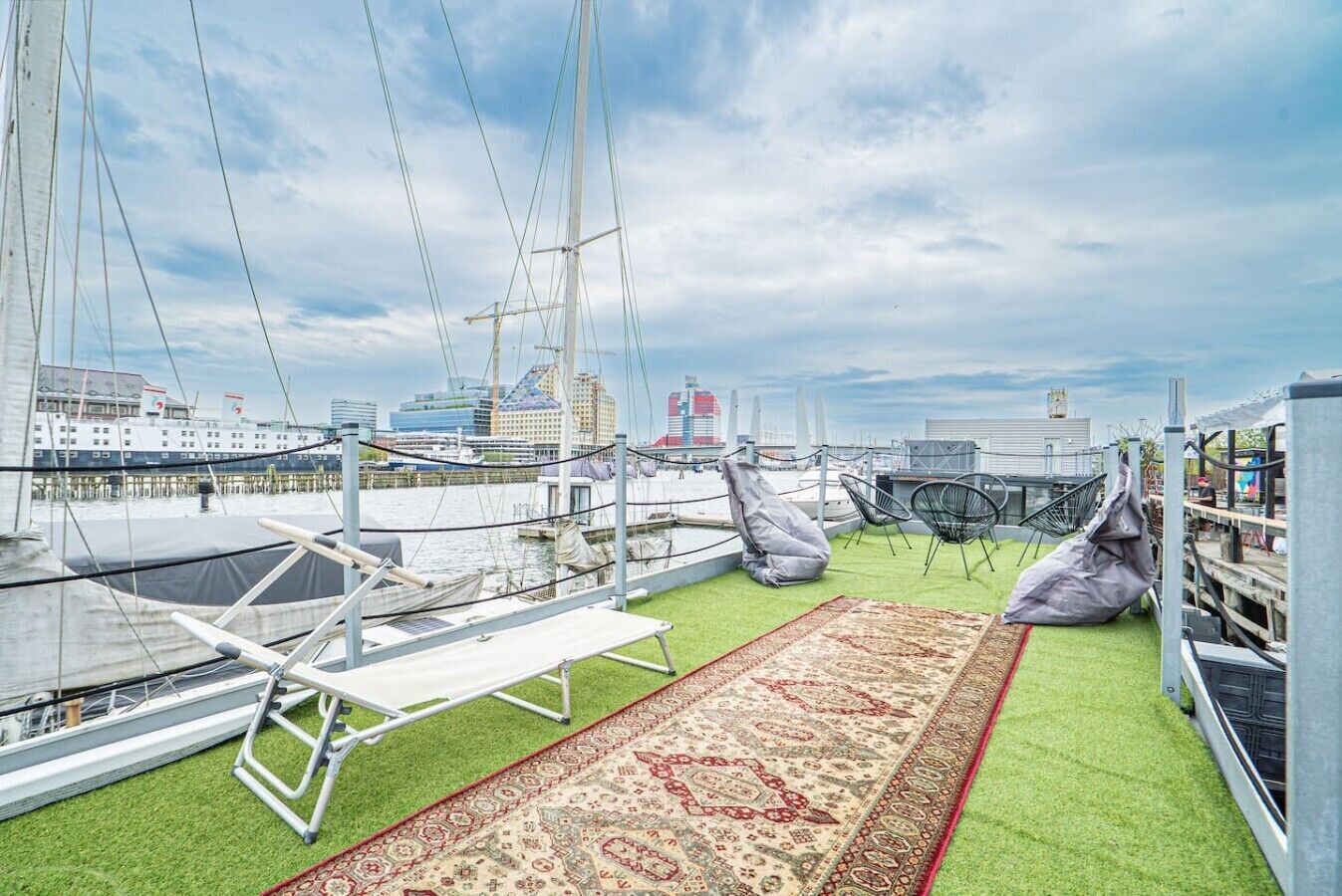 Una terrazza sul tetto con erba sintetica, un tappeto decorato, zone relax e vista sul porto turistico e sugli edifici.