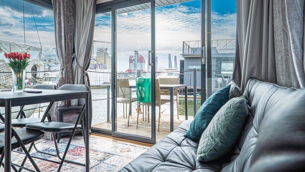 Et moderne værelse med stor skydedør, sofa, spisebord og udsigt til lystbådehavnen.
