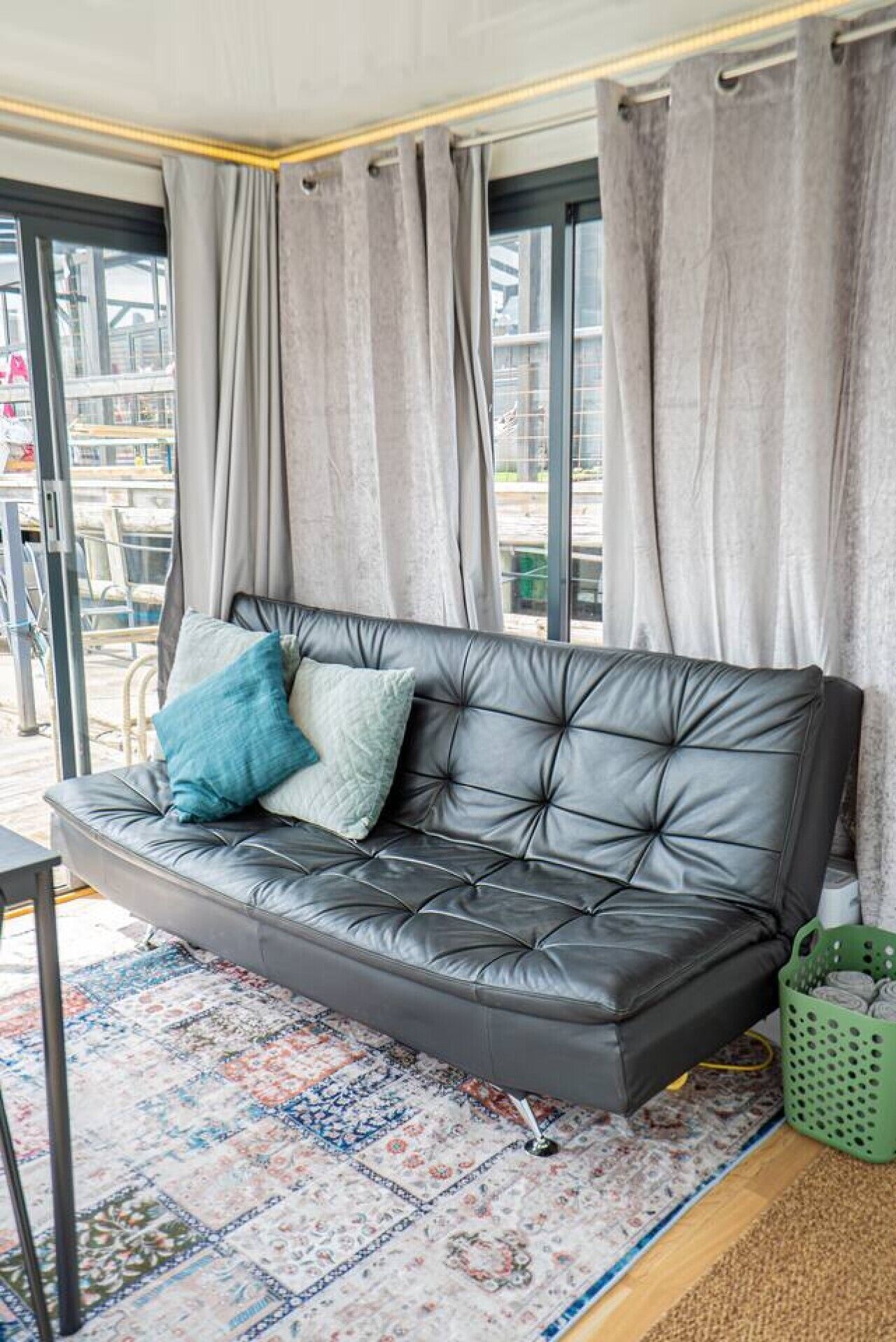 Un canapé en cuir noir avec deux coussins, un tapis à motifs et un panier vert.