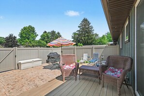 A covered patio with wicker furniture, a grill, and a colorful umbrella. - Bright Condo with Fire pit—Near Beach & Town (Douglas)
