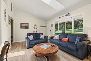 A spacious living room with two sofas, a coffee table, and a view of a garden through large windows. - Bright Condo with Fire pit—Near Beach & Town (Douglas)