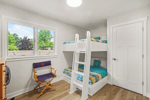 Ein Zimmer mit Etagenbetten, einem Fenster mit Blick auf Bäume, einem Ventilator und einer Tür.