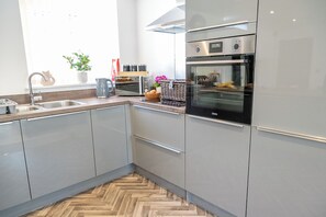 A modern kitchen with stainless steel appliances, a herringbone wood floor, and a window with natural light.