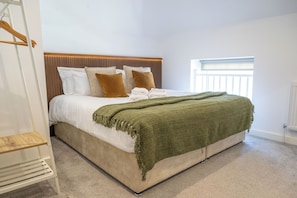 A neatly made bed with a green blanket, a wooden headboard, and a white radiator. - 2-Bed Retreat- Gated Parking- Work, Recharge, Stay (Worksop)
