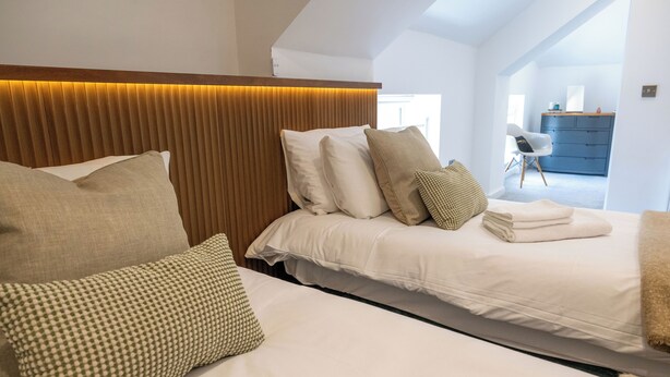 Una camera da letto con un letto, cuscini, testiera e vista su un corridoio.