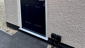 Una porta nera con stipite bianco, una targa con il numero civico e un lampadario fissato al muro.