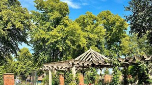 Un parco con una pergola in legno, una panchina e fiori rossi in fiore.