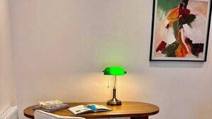 Una stanza con un tavolo rotondo in legno, una lampada da scrivania verde, una sedia e un quadro astratto appeso al muro.