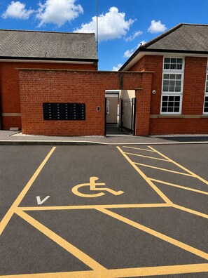 A parking area with a wheelchair accessibility symbol, a building entrance with a brick facade, and a clear blue sky.