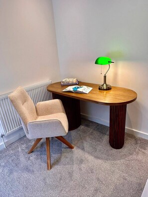 A small, cozy room with a round wooden table, a single chair, a radiator, and a green desk lamp. - 2-Bed Retreat- Gated Parking- Work, Recharge, Stay (Worksop)