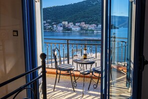 Uma varanda com mesa e cadeiras, uma garrafa de vinho e vista para um lago com edifícios ao fundo.