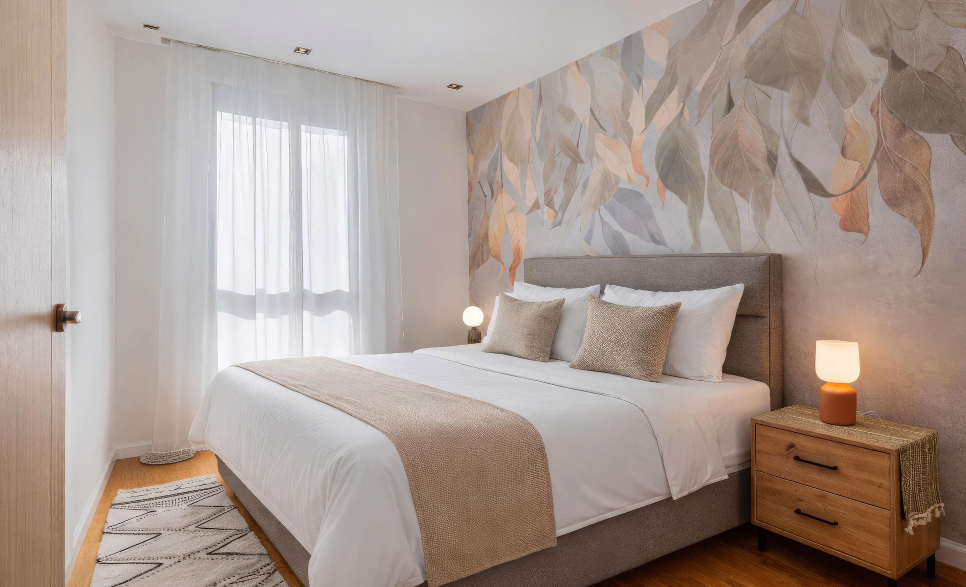 A bedroom with a bed, bedside tables, a nightstand, a lamp, and a window with sheer curtains.