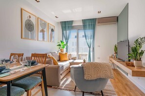 Ein modernes Wohnzimmer mit Essbereich, einer Couch, einem Fernseher und einem Balkon mit Vorhängen.