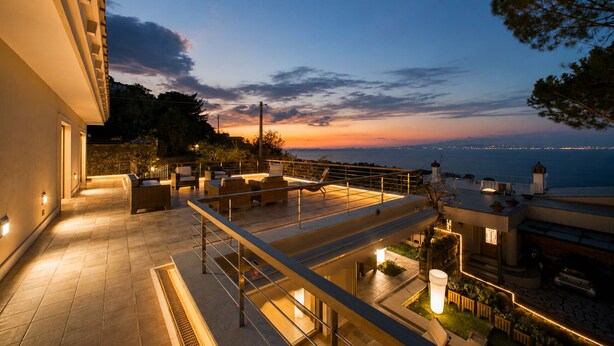 Eine Dachterrasse mit Sitzgelegenheiten im Freien, Blick aufs Meer und einer gut ausgeleuchteten Architektur.