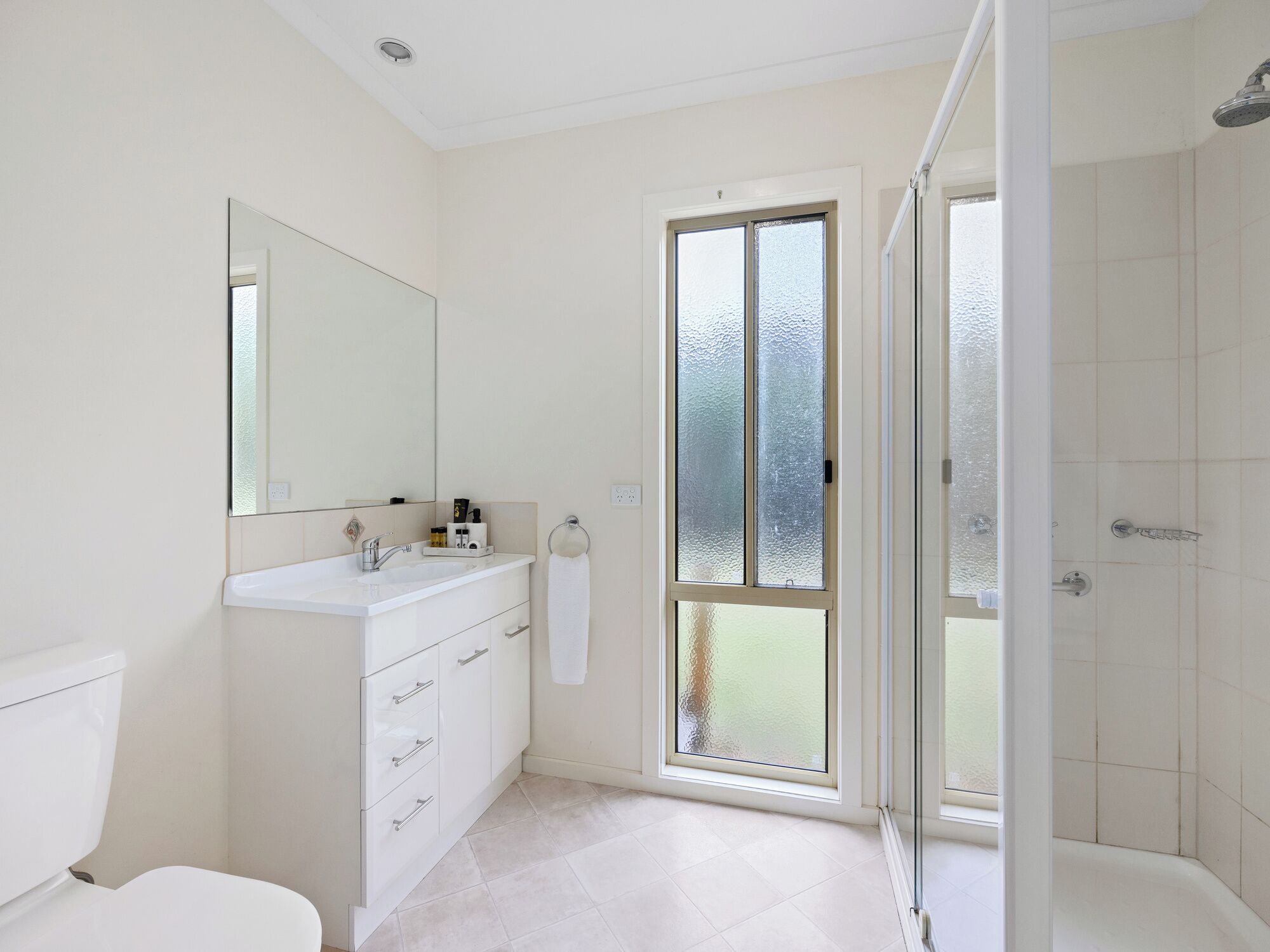 Une salle de bain moderne avec un meuble-lavabo blanc, un grand miroir, des toilettes et une porte de douche en verre.