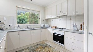 Eine moderne Küche mit weißen Schränken, einem Gasherd, einem Backofen und einem Fenster mit Blick auf Grünflächen.