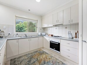 A modern kitchen with white cabinets, a gas stove, a built-in oven, and a window with a view of greenery. - Marysville River Retreat (Marysville)