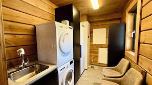 Ein gemütlicher, holzgetäfelter Raum im Blockhausstil mit Waschmaschine, Spüle, Kühlschrank und einem Sessel.