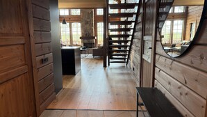 Een houten interieur met een open haard, een trap en uitzicht door grote ramen.