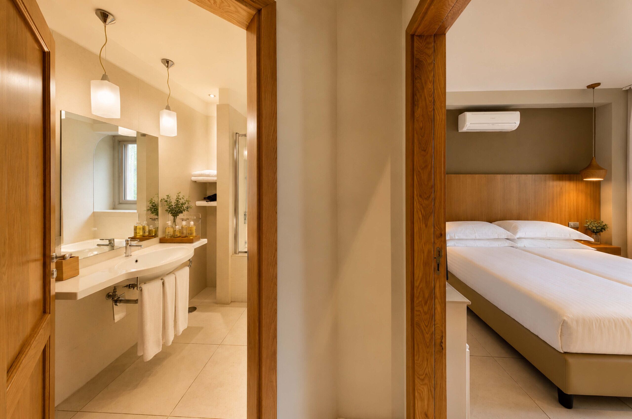 A modern hotel room with a wooden floor, a large bed, a bedside table, a nightstand, a mirror, a sink, and a towel rack.