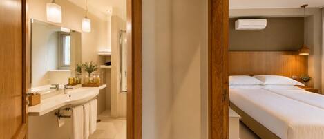 A modern hotel room with a wooden floor, a large bed, a bedside table, a nightstand, a mirror, a sink, and a towel rack.
