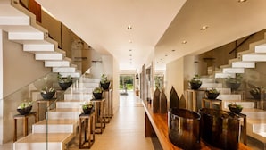 Un interior moderno con escalera, barandillas de cristal y plantas en macetas.