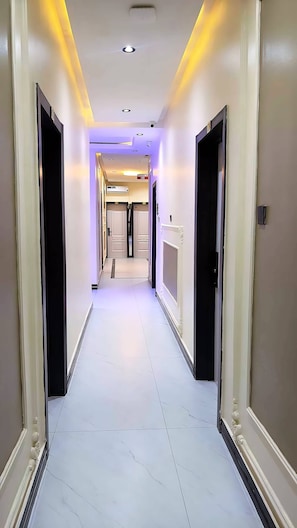 Un pasillo de hotel con puertas a ambos lados, suelo de baldosas e iluminación empotrada en el techo.