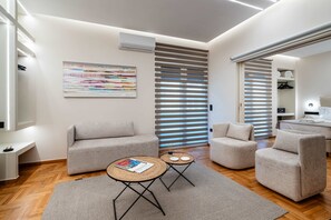 A modern living room with two sofas, a coffee table, and a large window with blinds. - Apex B1 - Modern City Stay in Central Pangrati (Athens)