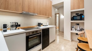 A compact kitchen with wooden cabinets, a microwave, a coffee maker, and a dishwasher. - Apex B1 - Modern City Stay in Central Pangrati (Athens)