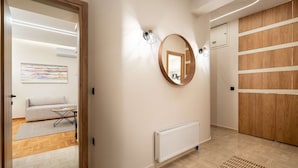 A modern hallway with a wooden door, a round mirror, a radiator, and a light fixture. - Apex B1 - Modern City Stay in Central Pangrati (Athens)