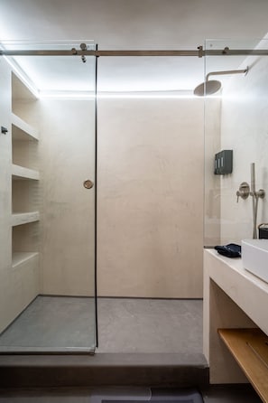 Ein modernes Badezimmer mit Duschkabine aus Glas, einem weißen Waschbecken und einem Holzregal.