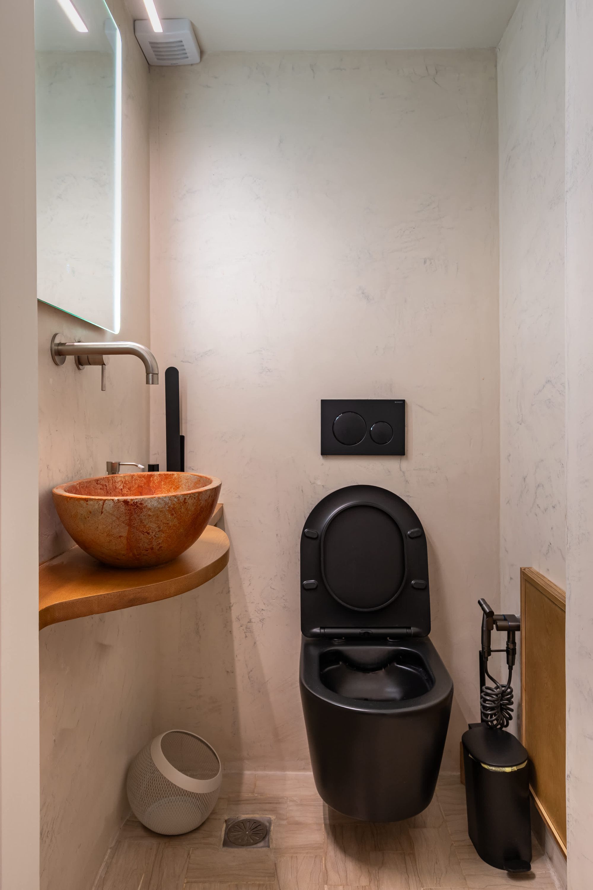 A bathroom with a large vessel sink, a black toilet, and a small trash bin.